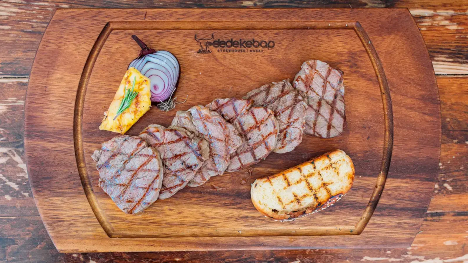 Kömür ateşinde ızgara edilmiş dana lokum dilimleri, közlenmiş ananas ve kırmızı soğan eşliğinde ahşap tahtada servis – Bakı Dede Kebap Steak Burger Tatlı Kasap