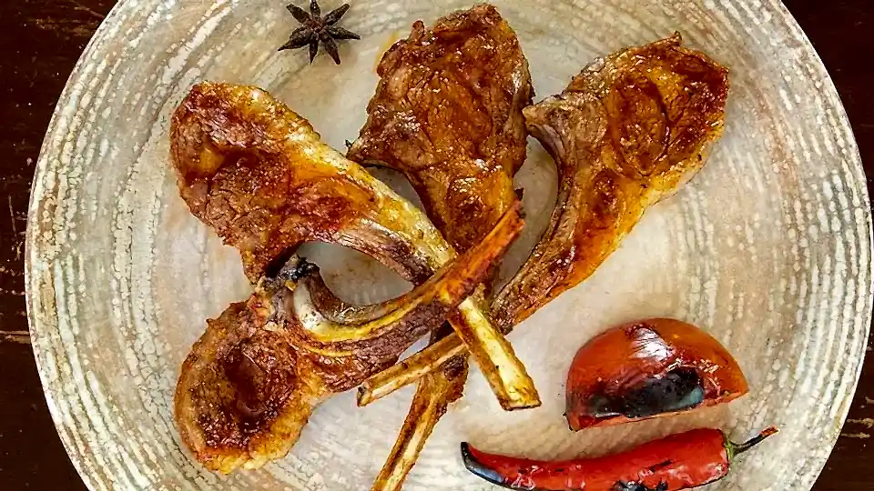 Kömür ateşinde ızgara edilmiş kuzu pirzola, yanında közlenmiş domates ve biber ile porsiyon sunum – Bakı Dede Kebap Steak Burger Tatlı Kasap